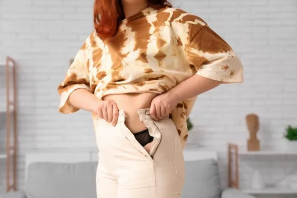 Image of woman trying to do her trousers up after pregnancy weight gain Harwich