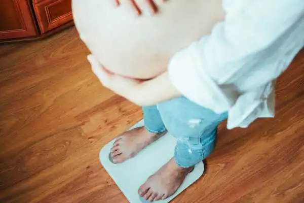 Image of woman weighing herself and experiencing weight gain through pregnancy Harwich